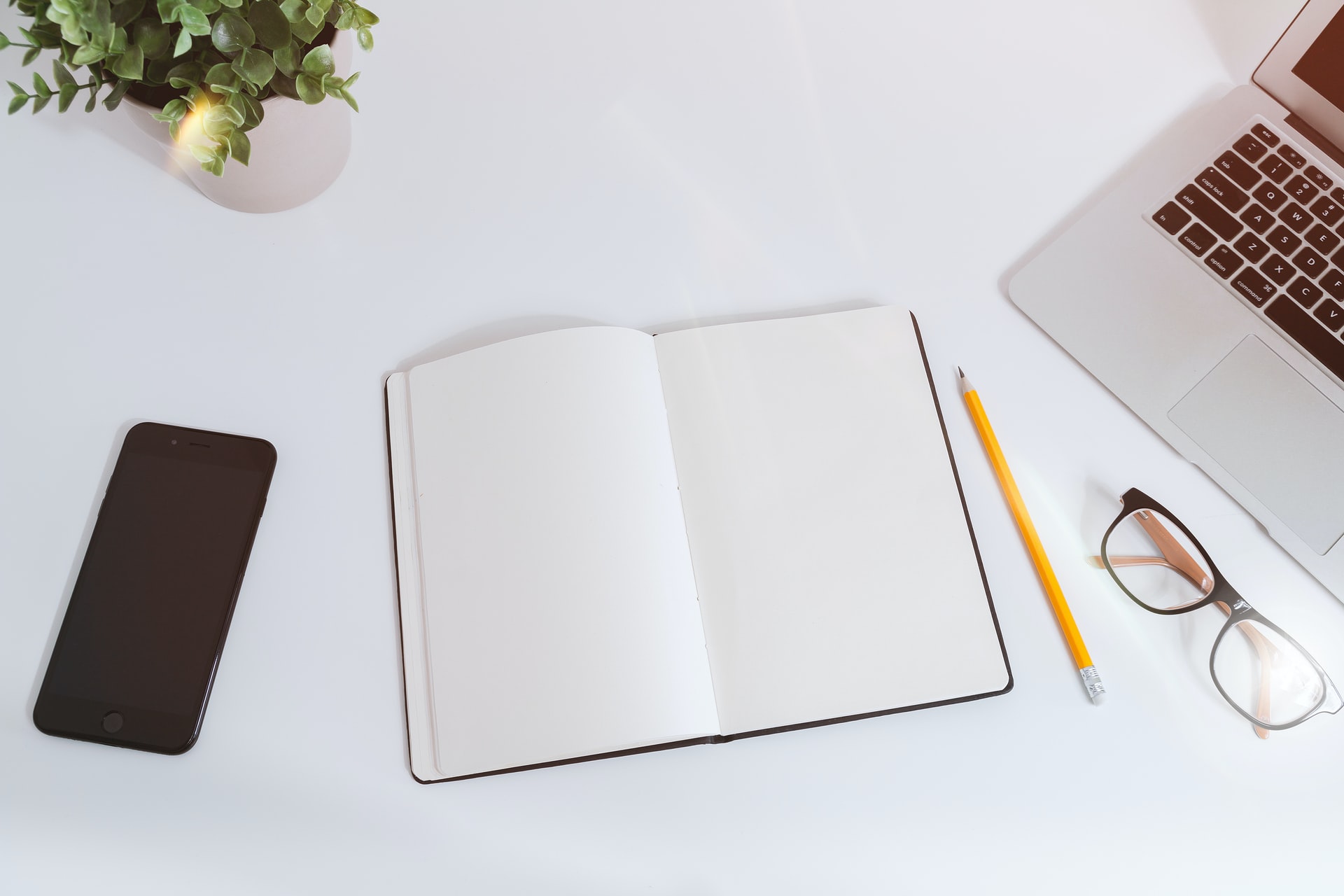 Notebook open with pencil and glasses at the side and an open laptop ready to write