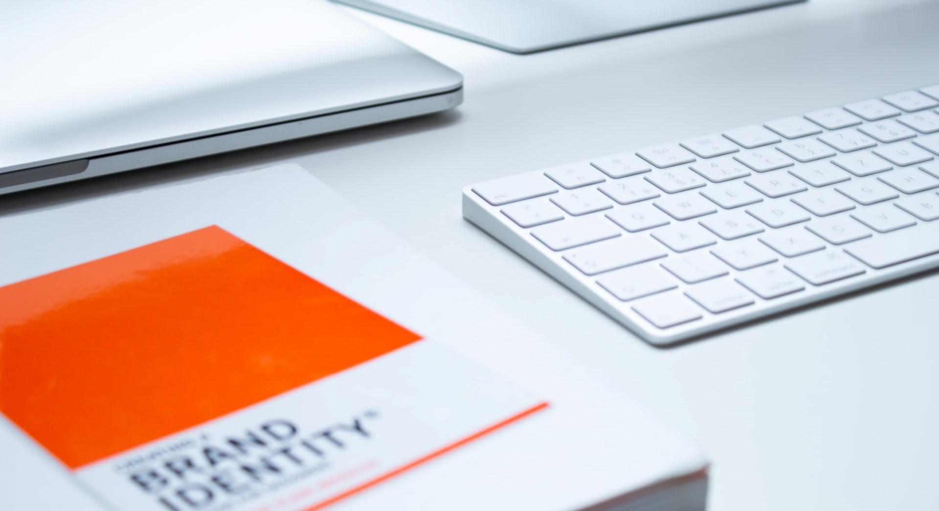 White desk with computer keyboard and screen, laptop and book labelled Brand Identity.