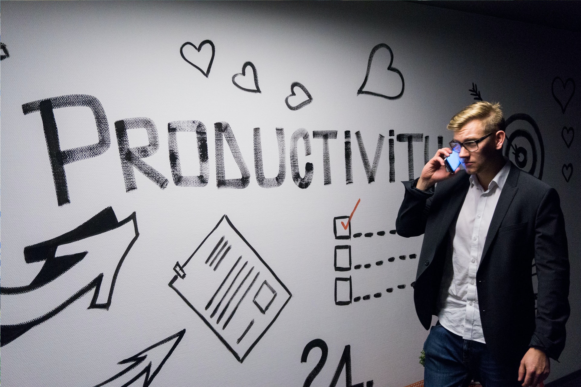Man on his mobile phone in front of a white board with the word productivity written across it with a tick box