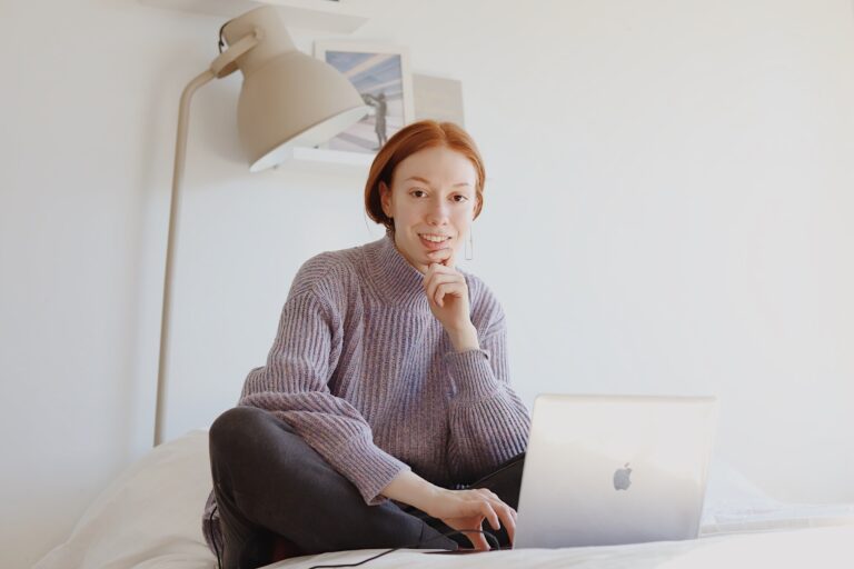Young woman sat on cushion crossed legged with an opened laptop in front of her