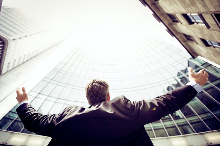 Business man with arms raised in front of office blocks