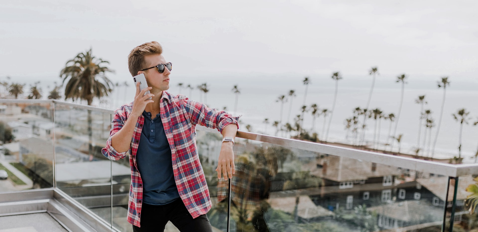 A man on a balcony overlooking a beach while speaking on his mobile phone