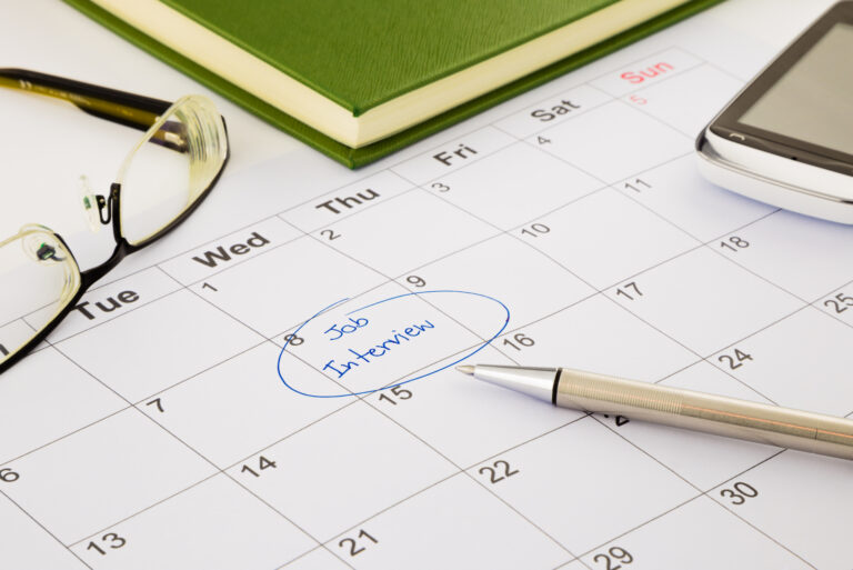 Calendar on desk with a Job Interview written in a date square and circled with a pen.