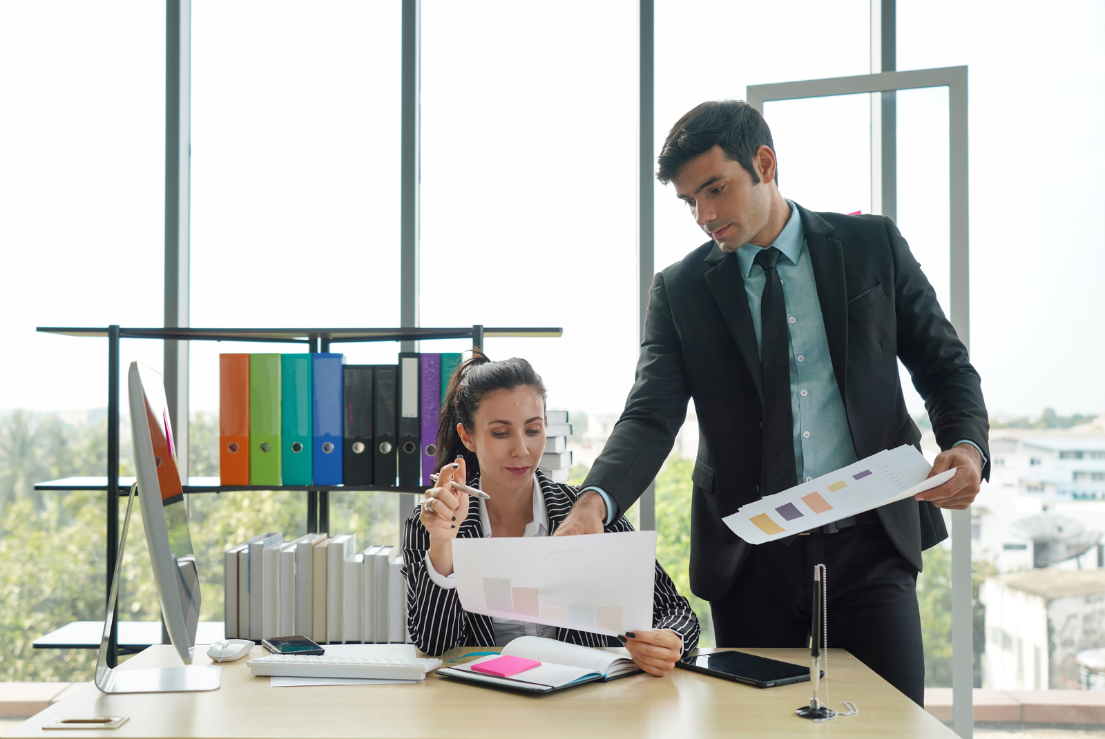 Professional business woman working in front of her laptop with professional business man leaning over and pointing at the screen.