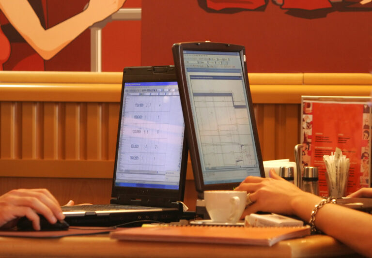 Two people working in a cafe with their laptops open on the table.