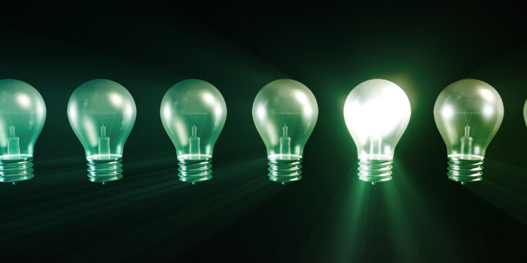six light bulbs in a line. One of the light bulbs is lit and shinning brightly next to the others to illustrate a creative idea.