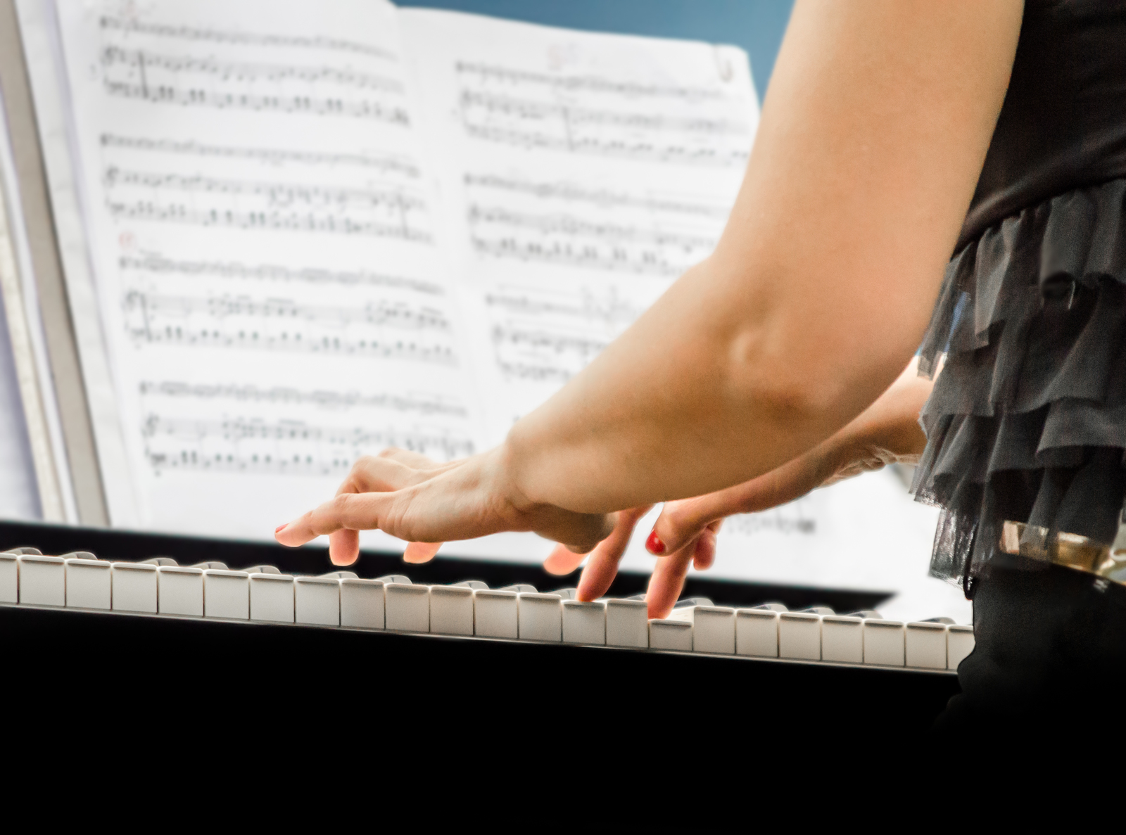 Young woman playing the piano with sheet music infront of her at a concert