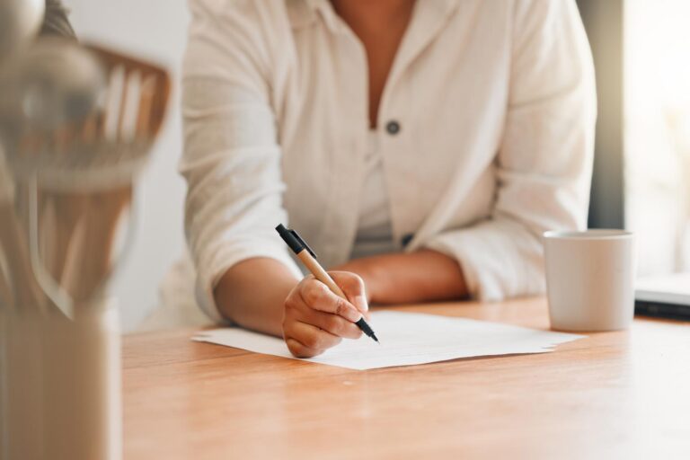 Woman sat at a desk with a mug of coffee and a pen and paper