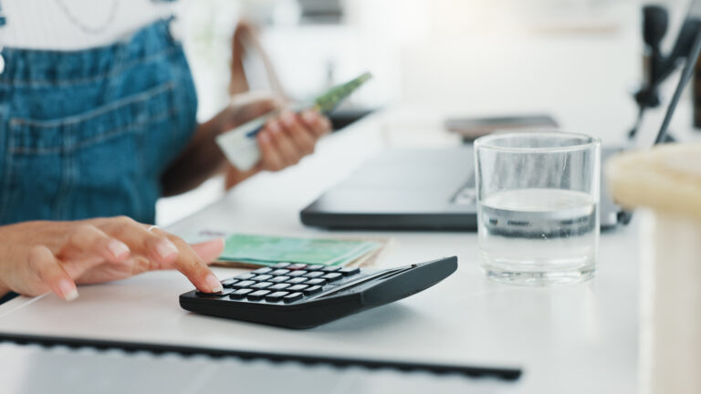 A business woman sat at her desk with a laptop, calulator and glass of water in front of her while doing the finances
