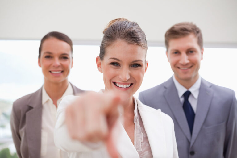 Two male business people and one female business person. The female is pointing towards the camera to indicated that you have been selected for the role.