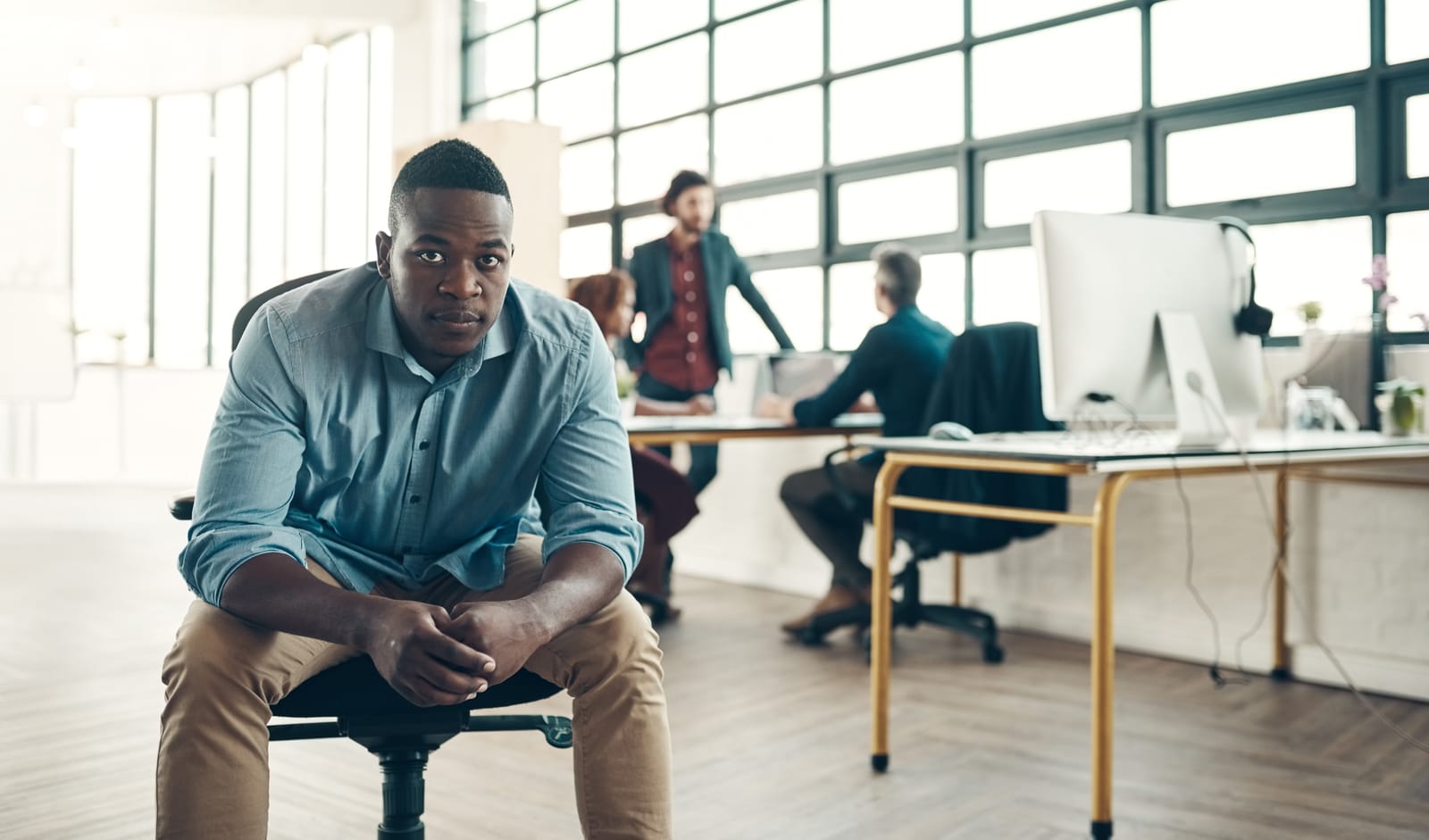 A tech business man sat on a office chair with a small team behind him