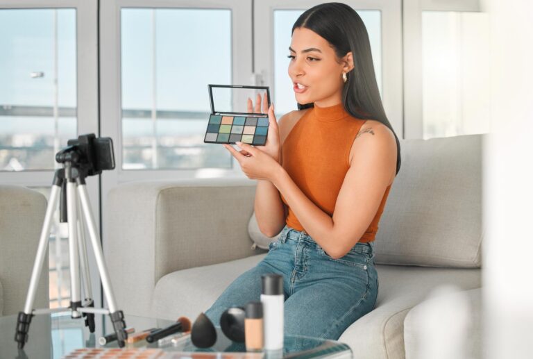 Young female influencer sitting in front of a camera promoting make up for a youtube video.