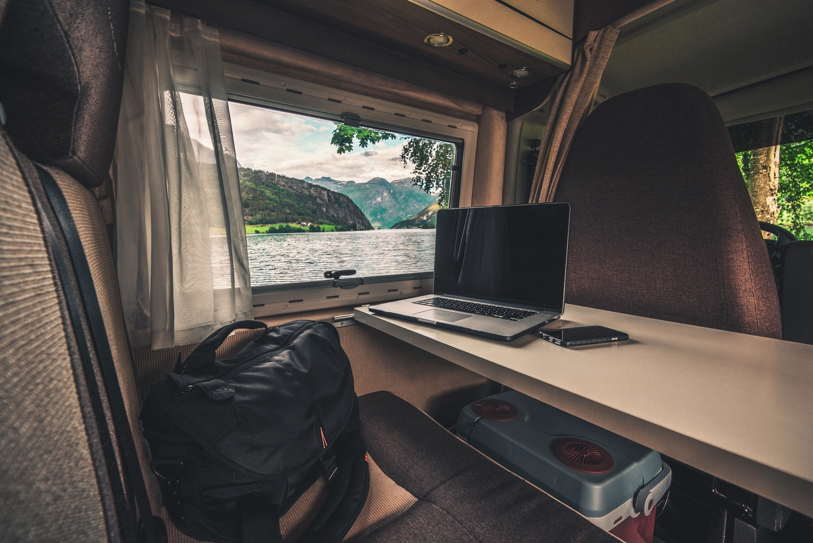 a laptop on a desk with a briefcase on the chair and an open window to the sea to illustrate work with travel.