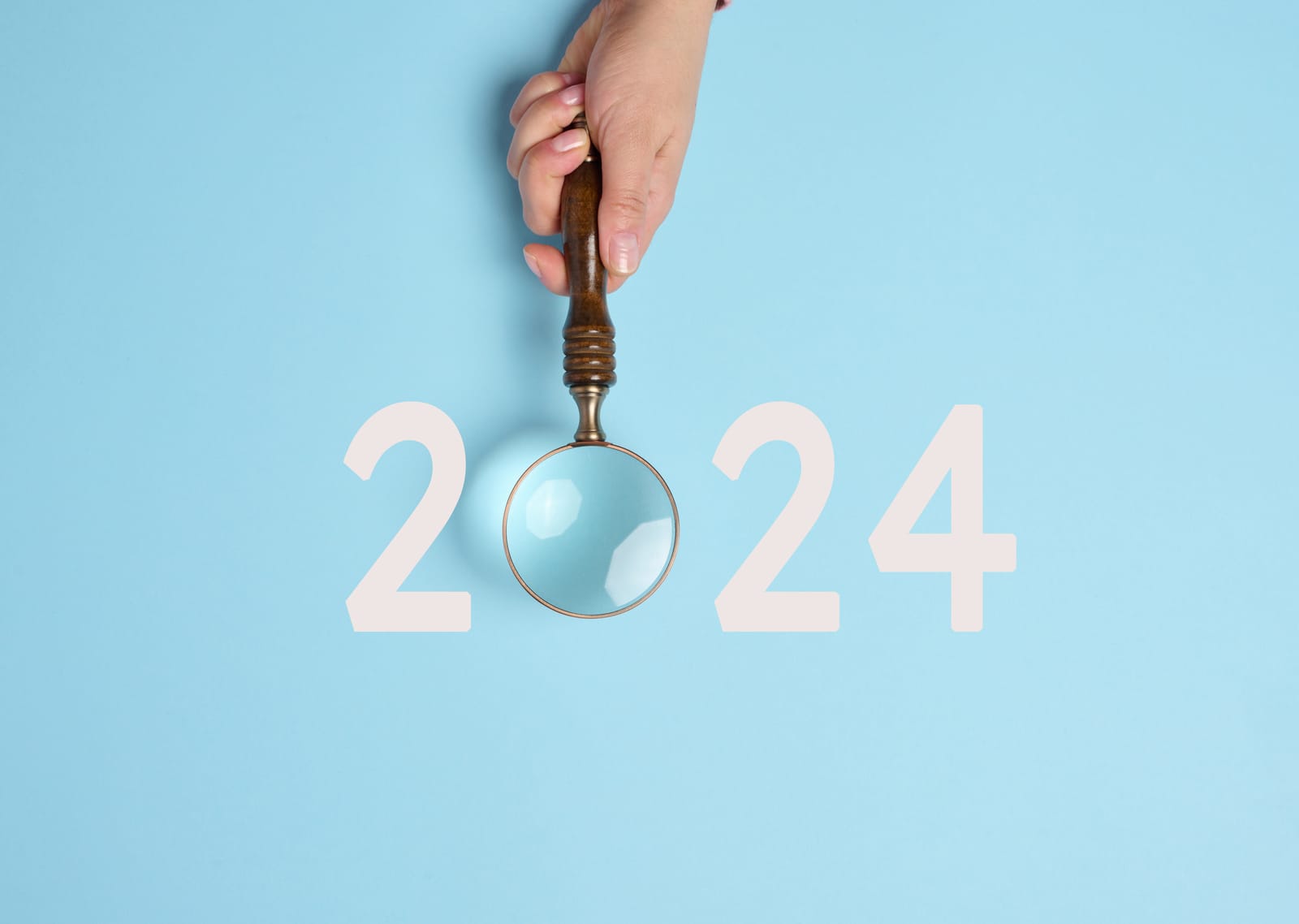 2024 on a blue background with a magnifying glass in place of the zero held by a female hand.