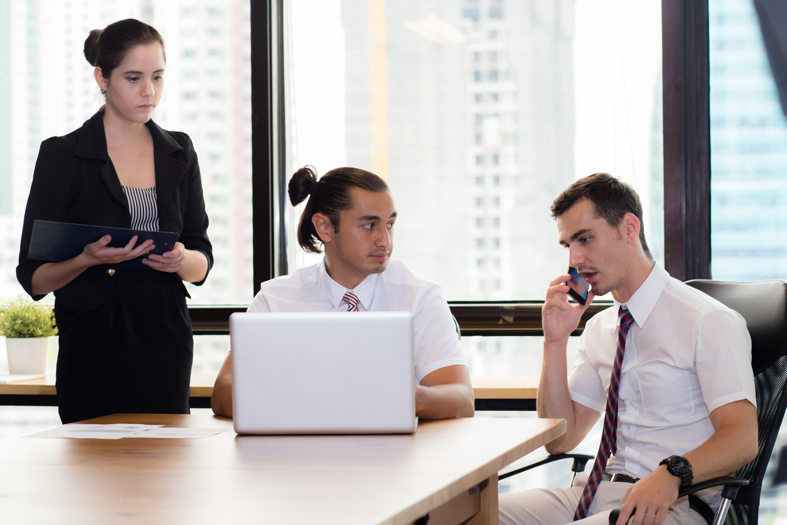 Woman stood holding ipad and looking on while two male employees are taking credit for her work