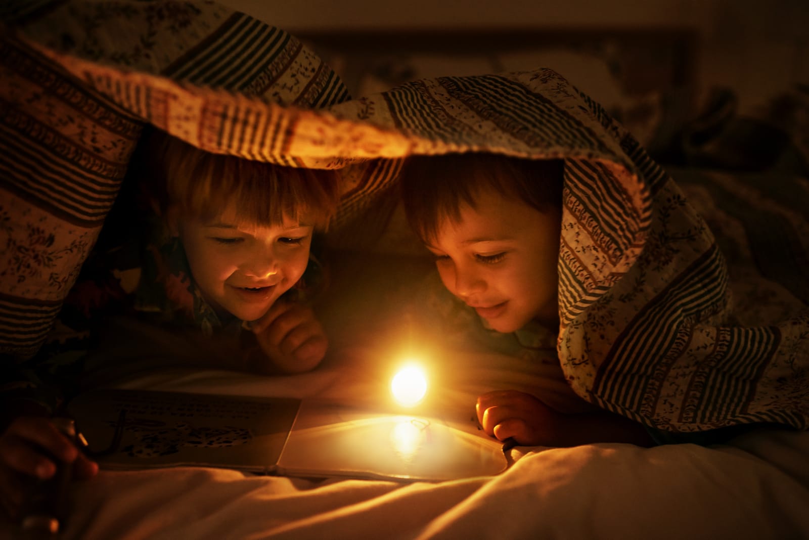 Two children under a blanket with a torch on watching a film telling a story.