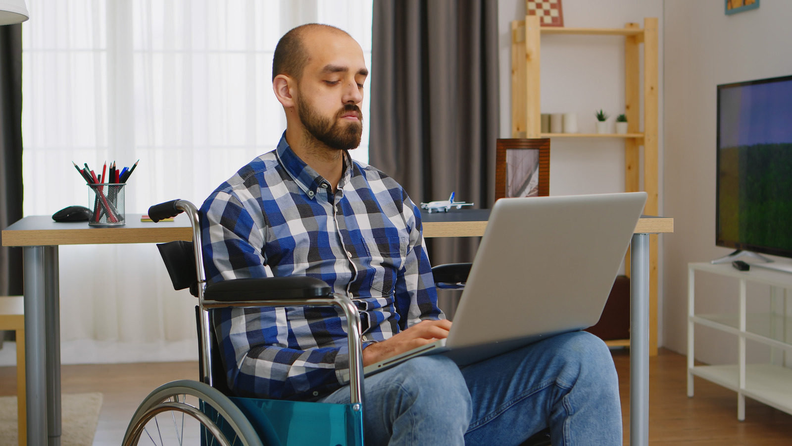 Disabled man in a wheelchair, buying stuff via a laptop on his lap.